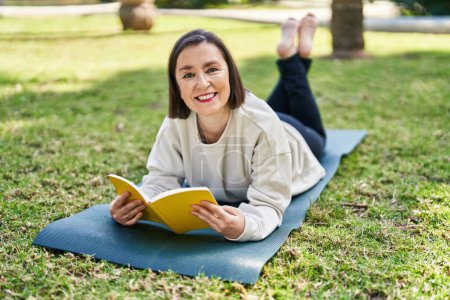 Téléchargez les photos : Femme d'âge moyen lecture livre couché sur herbe au parc - en image libre de droit