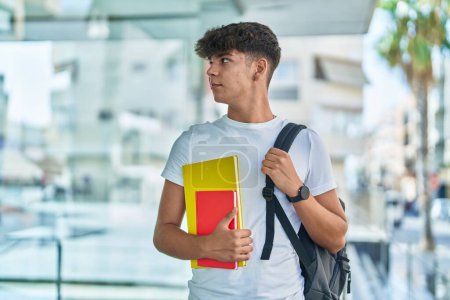 Téléchargez les photos : Jeune adolescent hispanique tenant des livres avec une expression détendue à l'université - en image libre de droit