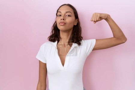 Photo for Young hispanic woman wearing casual white t shirt strong person showing arm muscle, confident and proud of power - Royalty Free Image