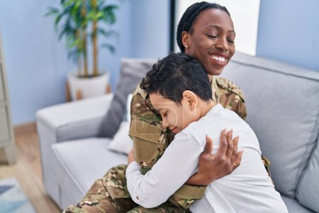Foto de African american mother and son wearing soldier uniform hugging each other at home - Imagen libre de derechos