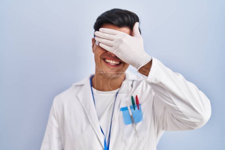 Photo for Hispanic man working as scientist smiling and laughing with hand on face covering eyes for surprise. blind concept. - Royalty Free Image