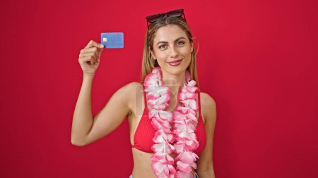 Foto de Joven rubia turista sosteniendo tarjeta de crédito sonriendo sobre fondo rojo aislado - Imagen libre de derechos