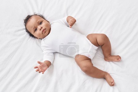 Téléchargez les photos : Bébé afro-américain se relaxant au lit dans la chambre - en image libre de droit