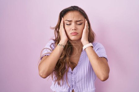 Foto de Mujer hispana joven de pie sobre fondo rosa con la mano en la cabeza, dolor de cabeza porque el estrés. padecer migraña. - Imagen libre de derechos