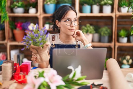 Photo for Young hispanic woman working at florist shop doing video call with hand on chin thinking about question, pensive expression. smiling with thoughtful face. doubt concept. - Royalty Free Image