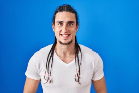 Photo for Hispanic man with long hair standing over blue background with a happy and cool smile on face. lucky person. - Royalty Free Image