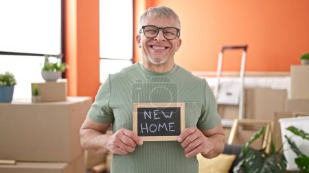 Téléchargez les photos : Moyen âge homme aux cheveux gris souriant confiant tenant tableau noir à la nouvelle maison - en image libre de droit
