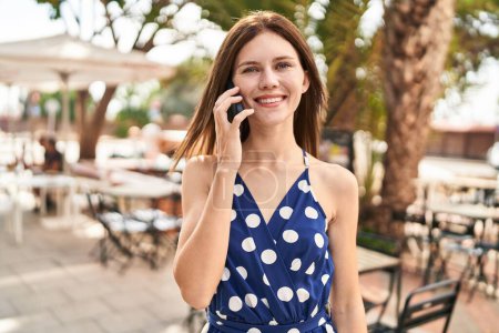 Téléchargez les photos : Jeune femme blonde souriante confiante parlant sur le smartphone à la terrasse du café - en image libre de droit