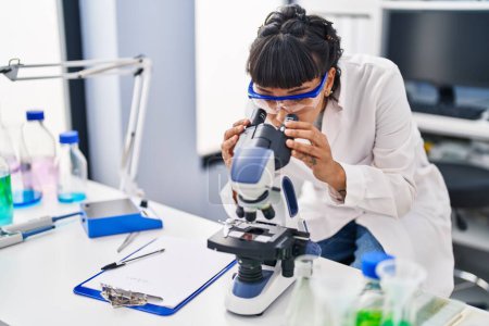 Téléchargez les photos : Jeune femme scientifique utilisant le microscope au laboratoire - en image libre de droit