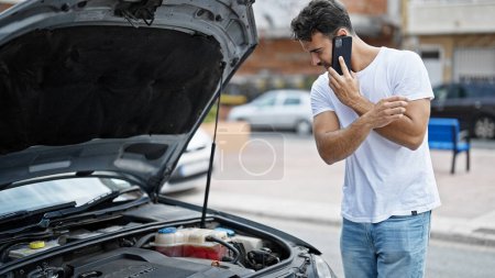 Photo for Young hispanic man talking on smartphone with insurance for car breakdown at street - Royalty Free Image