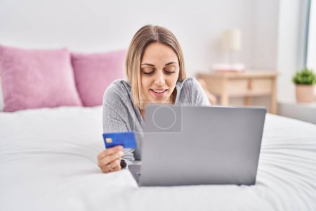 Photo for Young woman using laptop and credit card lying on bed at bedroom - Royalty Free Image