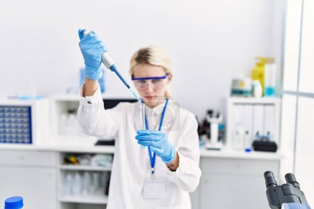 Téléchargez les photos : Jeune femme blonde scientifique versant du liquide sur éprouvette au laboratoire - en image libre de droit