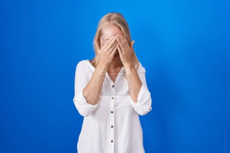 Foto de Young caucasian woman standing over blue background with sad expression covering face with hands while crying. depression concept. - Imagen libre de derechos