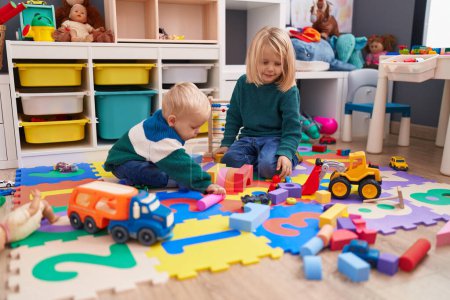 Téléchargez les photos : Adorable garçon et fille jouant avec des blocs de construction assis sur le sol à la maternelle - en image libre de droit