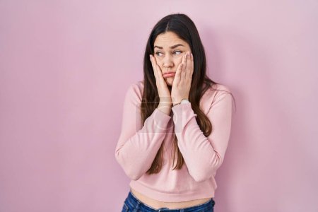 Foto de Young brunette woman standing over pink background tired hands covering face, depression and sadness, upset and irritated for problem - Imagen libre de derechos