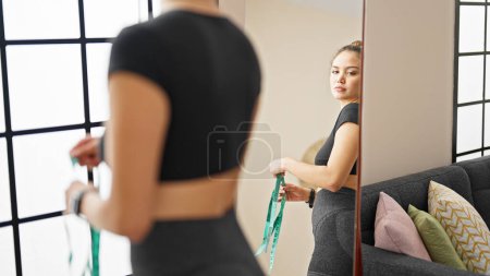 Photo for Young beautiful hispanic woman wearing sportswear measuring waist at home - Royalty Free Image