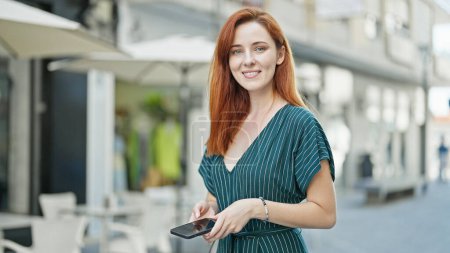 Photo for Young redhead woman using smartphone smiling at coffee shop terrace - Royalty Free Image