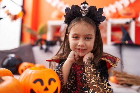 Foto de Adorable chica hispana con disfraz de halloween sosteniendo canasta de calabaza en casa - Imagen libre de derechos