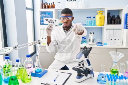 Foto de Hombre afroamericano trabajando en laboratorio libre de crueldad señalando con el dedo a la cámara y a ti, gesto confiado que parece serio - Imagen libre de derechos