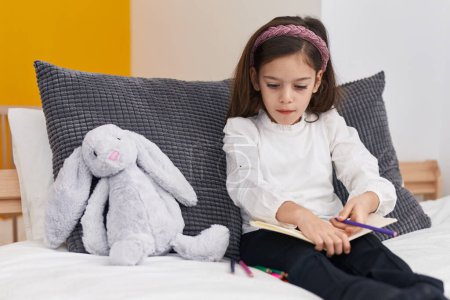 Photo for Adorable hispanic girl drawing on notebook sitting on bed at bedroom - Royalty Free Image