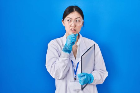 Photo for Chinese young woman working at scientist laboratory thinking worried about a question, concerned and nervous with hand on chin - Royalty Free Image