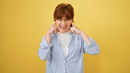 Foto de Mujer de mediana edad que cubre las orejas para el ruido sobre fondo amarillo aislado - Imagen libre de derechos