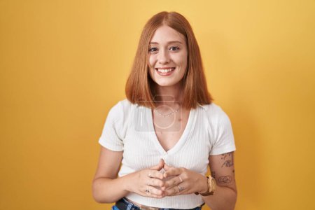 Téléchargez les photos : Jeune rousse femme debout sur fond jaune mains ensemble et les doigts croisés souriant détendu et joyeux. succès et optimisme - en image libre de droit
