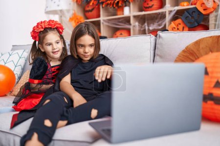 Téléchargez les photos : Adorable garçon et fille portant costume d'Halloween regarder film sur ordinateur portable à la maison - en image libre de droit
