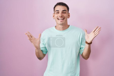 Téléchargez les photos : Bel homme hispanique debout sur fond rose célébrant fou et étonné pour le succès avec les bras levés et les yeux ouverts hurlant excité. concept gagnant - en image libre de droit