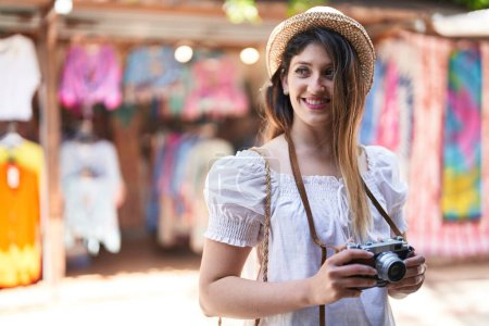 Téléchargez les photos : Jeune femme hispanique touriste souriant confiant en utilisant la caméra au marché de rue - en image libre de droit