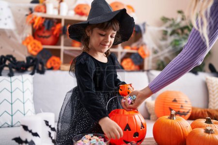 Téléchargez les photos : Adorable fille hispanique ayant fête d'Halloween recevoir des bonbons à la maison - en image libre de droit