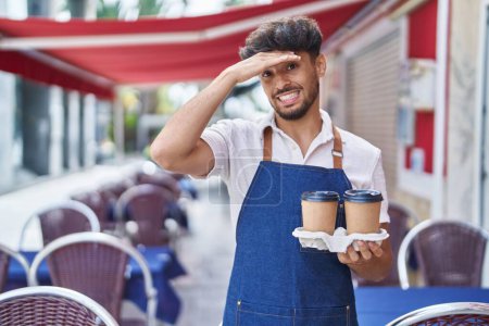 Foto de Arab man with beard wearing waiter apron at restaurant terrace stressed and frustrated with hand on head, surprised and angry face - Imagen libre de derechos