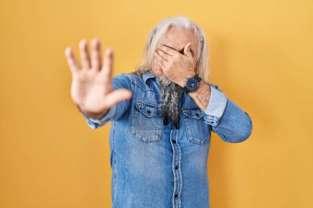 Photo for Middle age man with grey hair standing over yellow background covering eyes with hands and doing stop gesture with sad and fear expression. embarrassed and negative concept. - Royalty Free Image