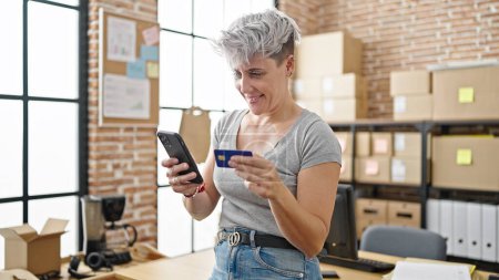 Foto de Mujer joven comercio electrónico trabajador de compras con teléfono inteligente y tarjeta de crédito en la oficina - Imagen libre de derechos