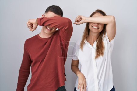 Téléchargez les photos : Mère et fils debout ensemble sur un fond isolé couvrant les yeux avec le bras souriant gai et drôle. concept aveugle. - en image libre de droit