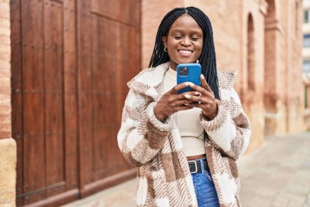 Téléchargez les photos : Afro-américaine femme souriant confiant en utilisant smartphone à la rue - en image libre de droit