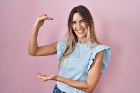 Photo for Young hispanic woman standing over pink background gesturing with hands showing big and large size sign, measure symbol. smiling looking at the camera. measuring concept. - Royalty Free Image