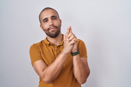 Photo for Hispanic man with beard standing over white background holding symbolic gun with hand gesture, playing killing shooting weapons, angry face - Royalty Free Image