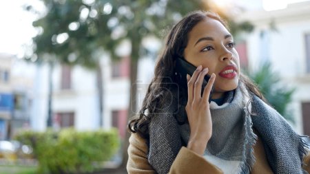 Téléchargez les photos : Jeune belle femme hispanique parlant sur smartphone avec une expression sérieuse au parc - en image libre de droit