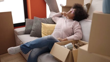 Foto de Mujer afroamericana joven sentada en un sofá relajándose en un nuevo hogar - Imagen libre de derechos