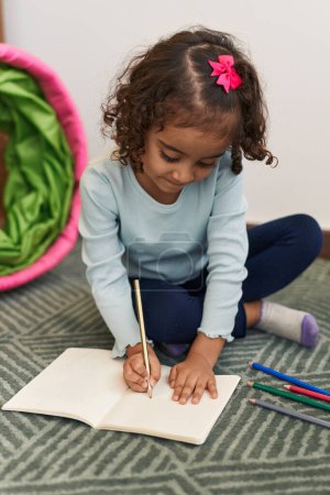 Photo for Adorable hispanic girl drawing on notebook sitting on floor at home - Royalty Free Image