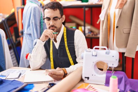 Téléchargez les photos : Jeune homme hispanique tailleur tenant des chiffons regardant carnet à l'atelier - en image libre de droit