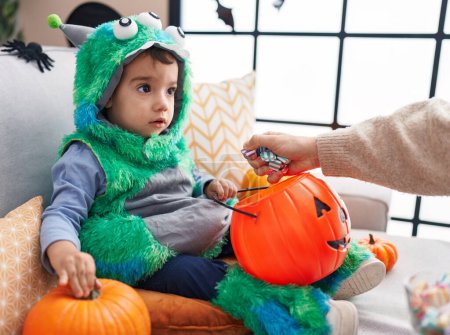 Foto de Adorable chico hispano teniendo fiesta de halloween sosteniendo dulces en casa - Imagen libre de derechos