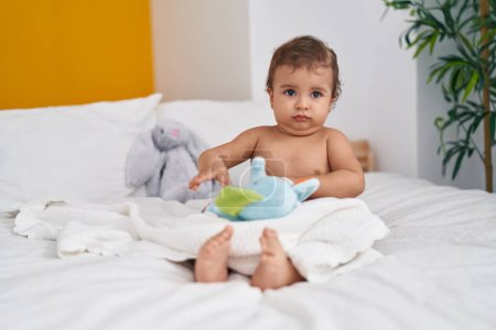 Photo for Adorable hispanic baby sitting on bed playing with elephant doll at bedroom - Royalty Free Image