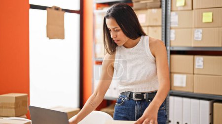 Foto de Joven mujer hispana hermosa comercio electrónico trabajador de negocios de pie hacia atrás en la oficina - Imagen libre de derechos