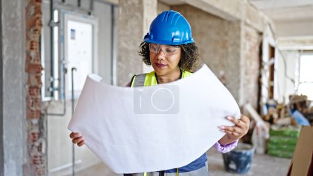 Photo for Young beautiful latin woman builder looking house project at construction site - Royalty Free Image