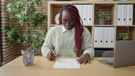 Photo for African woman with braided hair signing a document at office - Royalty Free Image