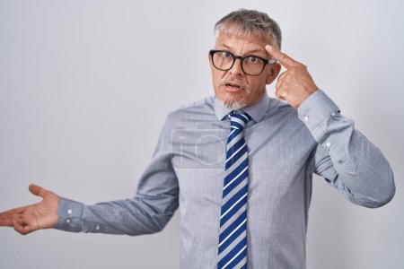 Téléchargez les photos : Homme d'affaires hispanique aux cheveux gris portant des lunettes confus et agacé avec la paume ouverte montrant l'espace de copie et pointant du doigt vers le front. Penses-y.. - en image libre de droit