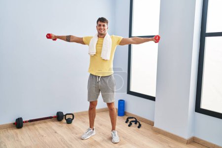 Téléchargez les photos : Young hispanic man smiling confident using dumbbells training at sport center - en image libre de droit