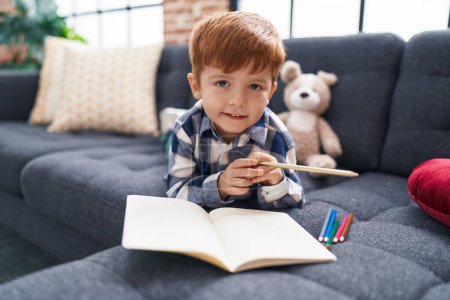 Téléchargez les photos : Adorable dessin d'enfant en bas âge sur ordinateur portable couché sur le canapé à la maison - en image libre de droit